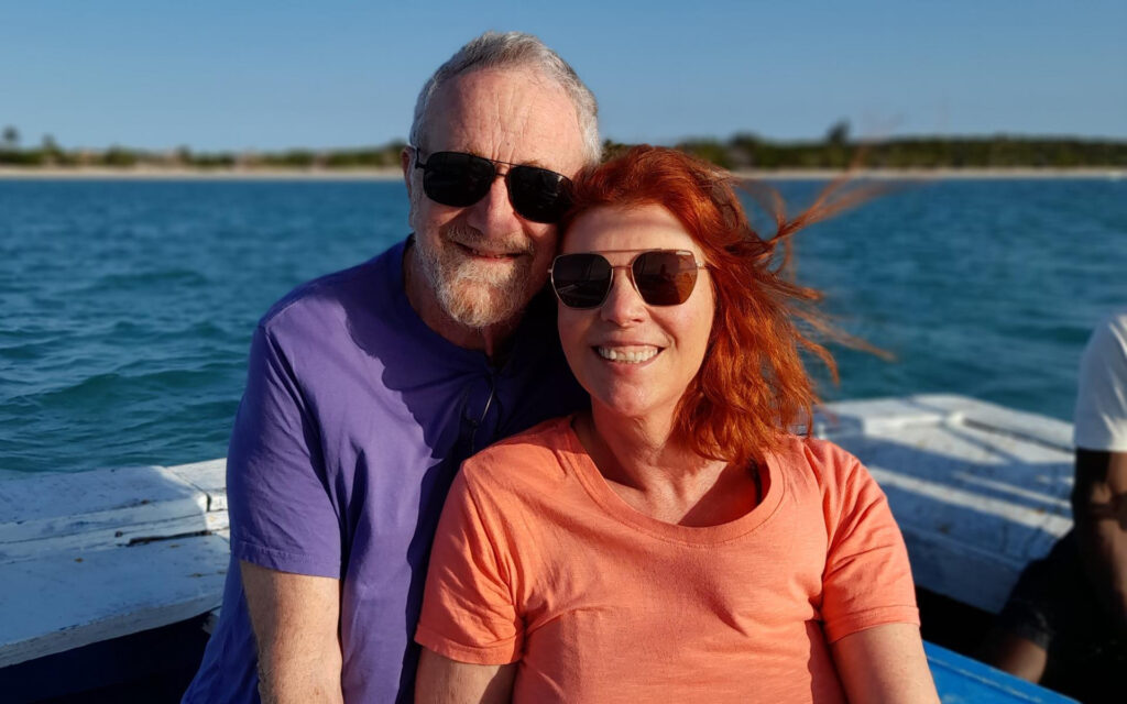 A woman sitting close to her partner on a dhow off the Mozambican coast; they are wearing sunglasses and smiling